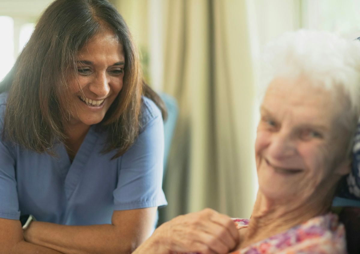 A smiling nurse sitting with an elderly woman in a bright room