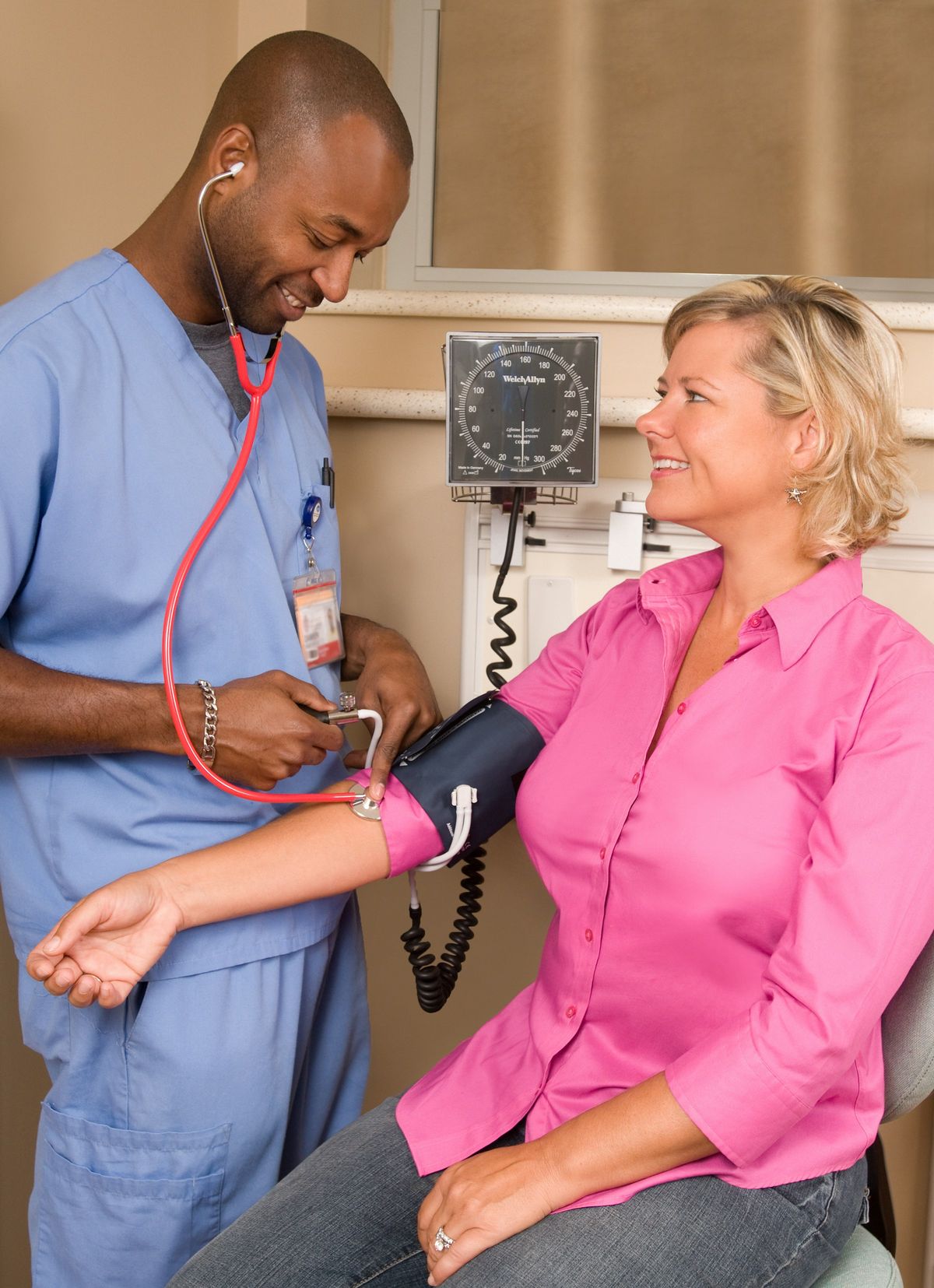 A male nurse in scrubs checking a smiling patient's blood pressure